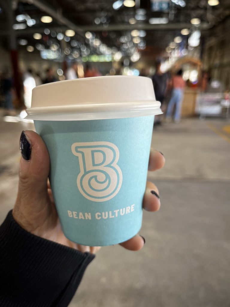 A take away coffee cup in a hand, with market behind